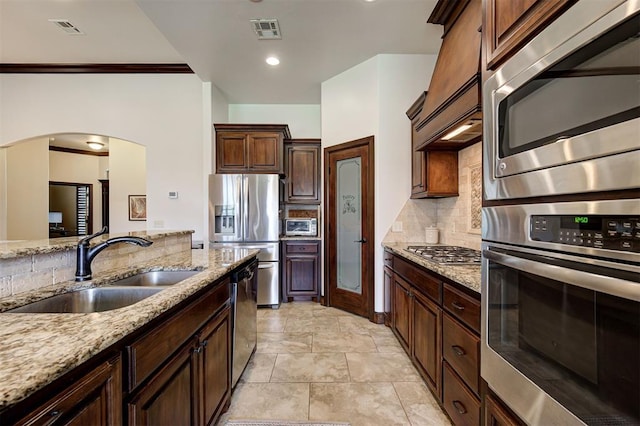 kitchen with sink, decorative backsplash, light stone countertops, ornamental molding, and appliances with stainless steel finishes