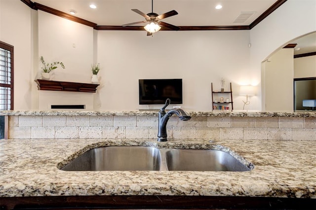 kitchen featuring crown molding, sink, ceiling fan, and light stone counters