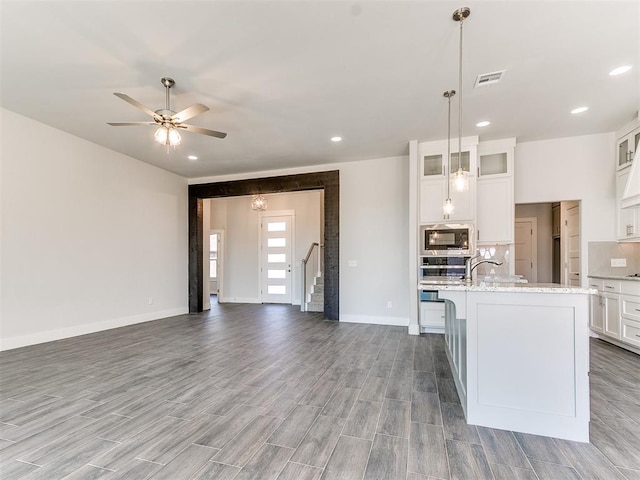 kitchen with stainless steel appliances, ceiling fan, decorative light fixtures, a center island with sink, and white cabinets