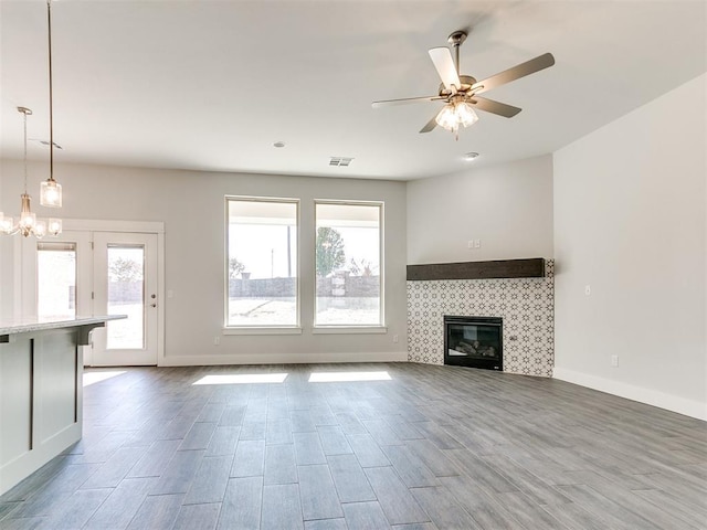 unfurnished living room with ceiling fan with notable chandelier, a fireplace, and a wealth of natural light