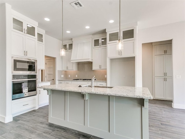 kitchen with a kitchen island with sink, hanging light fixtures, stainless steel appliances, and light stone counters