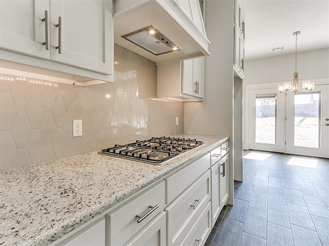 kitchen featuring custom exhaust hood, decorative backsplash, light stone counters, white cabinetry, and stainless steel gas cooktop