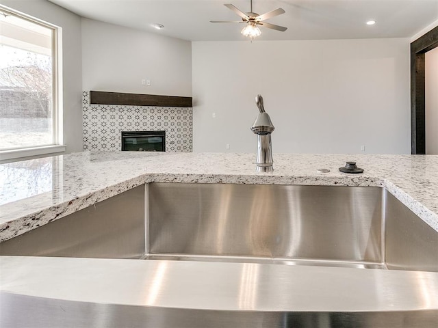 interior details with tasteful backsplash, light stone counters, ceiling fan, sink, and a fireplace