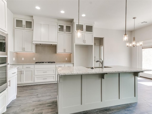 kitchen with sink, gas stovetop, light stone counters, decorative light fixtures, and a center island with sink