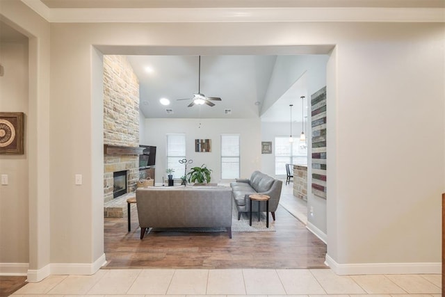 living room with a stone fireplace, ceiling fan, light tile patterned floors, and vaulted ceiling