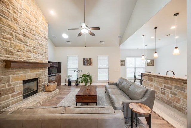 living room with a stone fireplace, ceiling fan, light hardwood / wood-style flooring, and high vaulted ceiling