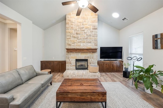 living room with a stone fireplace, ceiling fan, light hardwood / wood-style floors, and vaulted ceiling