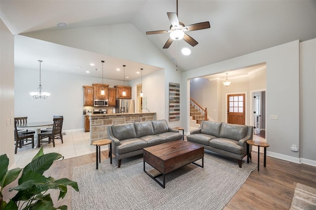 living room with high vaulted ceiling, ceiling fan with notable chandelier, and light hardwood / wood-style flooring