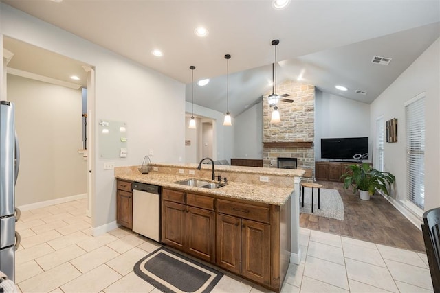 kitchen featuring sink, stainless steel appliances, light stone counters, a fireplace, and decorative light fixtures