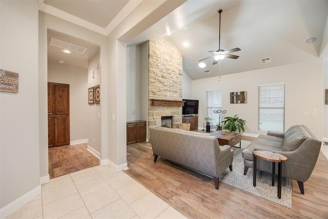 living room with ceiling fan, a stone fireplace, high vaulted ceiling, and light wood-type flooring