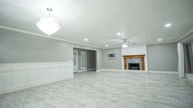 unfurnished living room with ceiling fan with notable chandelier, ornamental molding, and a fireplace