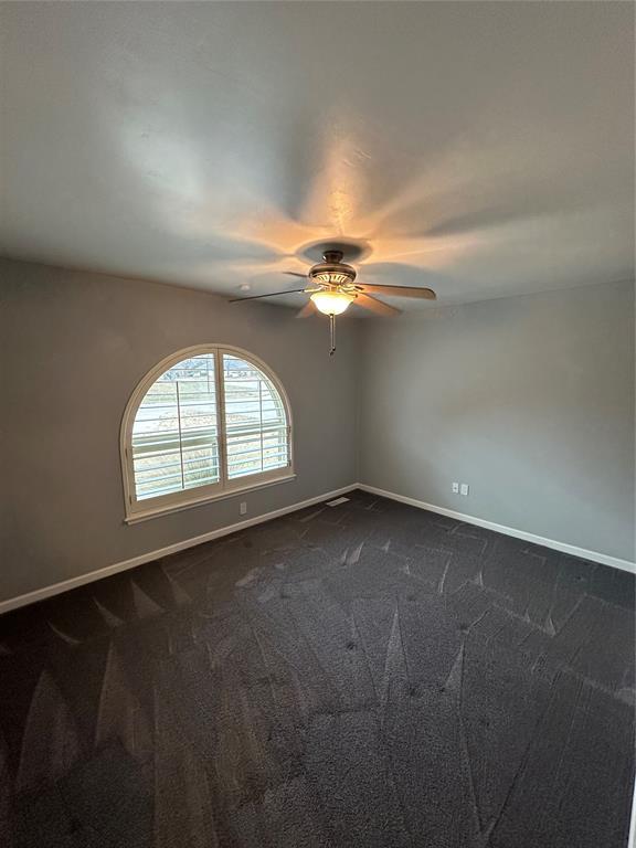 unfurnished room with dark colored carpet and ceiling fan