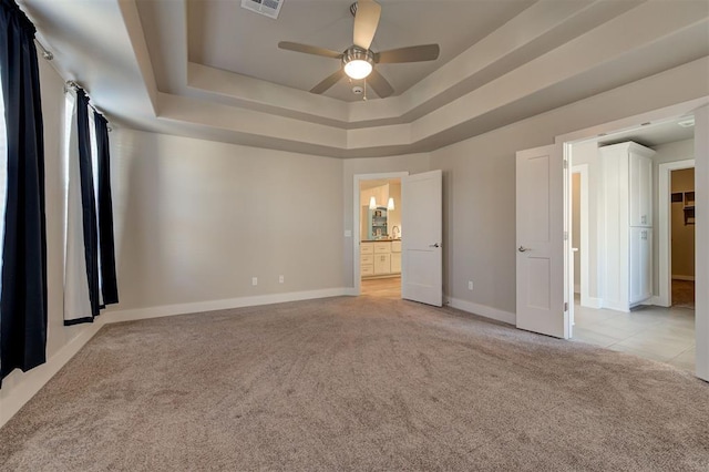 unfurnished bedroom featuring light carpet, connected bathroom, a tray ceiling, and ceiling fan