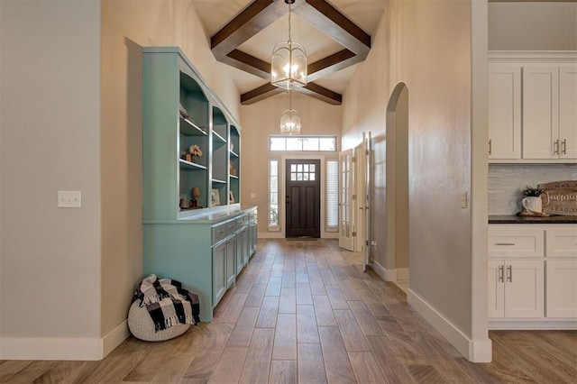 entryway featuring beam ceiling, light wood-type flooring, and a notable chandelier