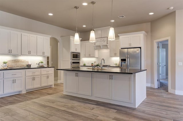 kitchen featuring white cabinetry, stainless steel appliances, decorative light fixtures, and a kitchen island with sink