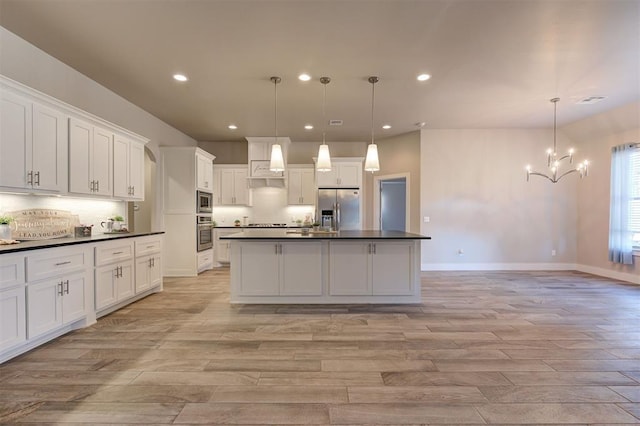 kitchen featuring white cabinetry, hanging light fixtures, a kitchen island with sink, stainless steel appliances, and light wood-type flooring