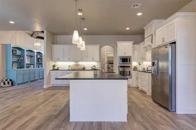 kitchen with appliances with stainless steel finishes, decorative light fixtures, tasteful backsplash, white cabinetry, and a center island with sink