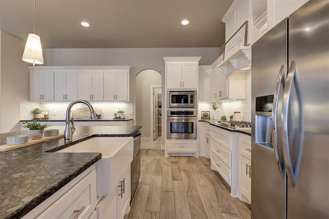 kitchen featuring appliances with stainless steel finishes, pendant lighting, white cabinetry, sink, and light hardwood / wood-style floors