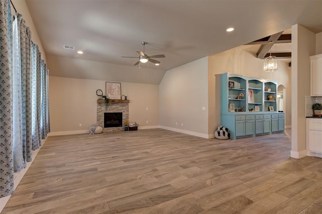 unfurnished living room featuring a stone fireplace, ceiling fan with notable chandelier, lofted ceiling, and light hardwood / wood-style floors