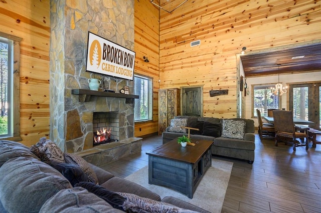 living room featuring a stone fireplace, dark hardwood / wood-style flooring, a notable chandelier, wood walls, and a towering ceiling