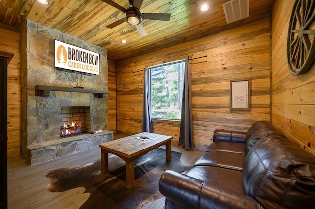 living room with wooden ceiling, a stone fireplace, wooden walls, hardwood / wood-style flooring, and ceiling fan