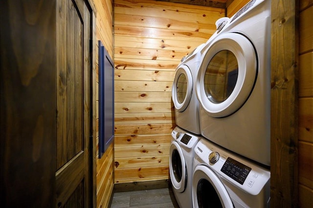 washroom featuring dark wood-type flooring, stacked washer / drying machine, and wood walls