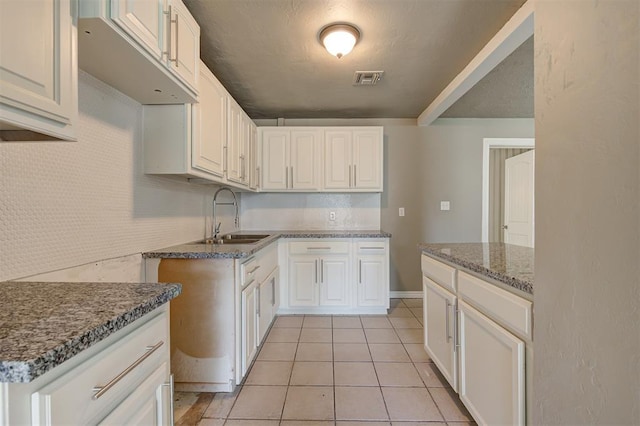 kitchen with white cabinets, light tile patterned floors, dark stone counters, and sink