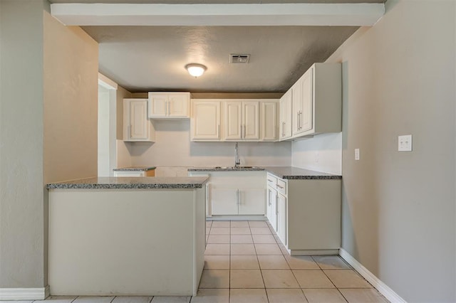 kitchen featuring white cabinets, sink, light tile patterned flooring, and dark stone counters