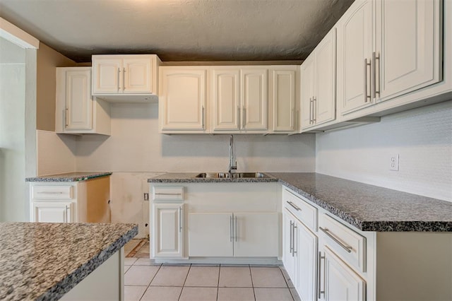 kitchen with light tile patterned flooring, white cabinetry, dark stone counters, and sink