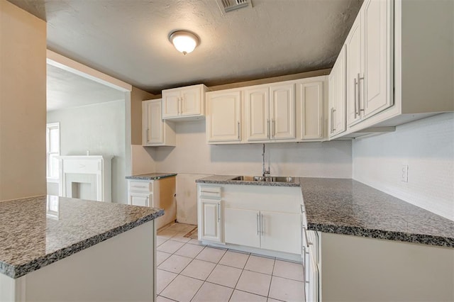 kitchen with sink, light tile patterned floors, dark stone counters, a textured ceiling, and white cabinets