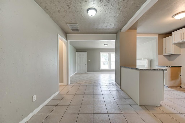 kitchen featuring kitchen peninsula, white cabinetry, dark stone countertops, and light tile patterned floors