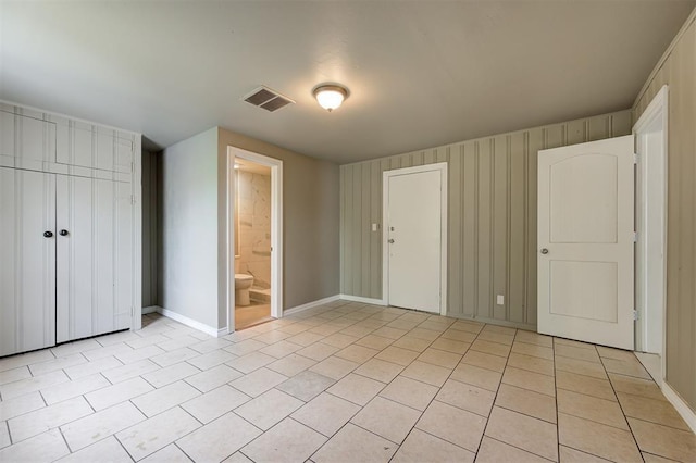 unfurnished bedroom with ensuite bath, a closet, and light tile patterned floors