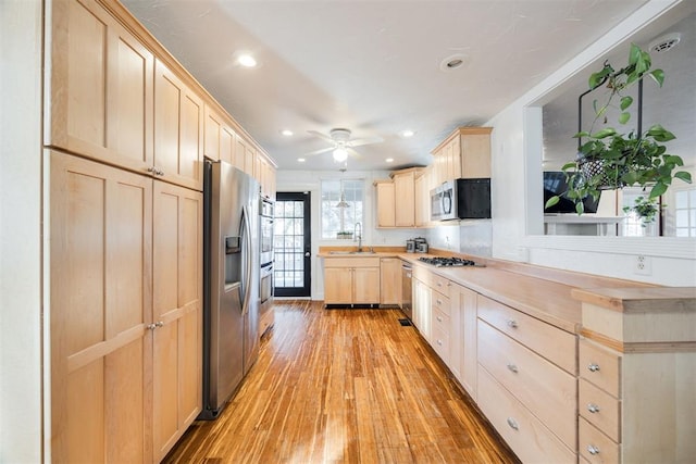 kitchen with light brown cabinetry, sink, light wood-type flooring, ceiling fan, and stainless steel appliances