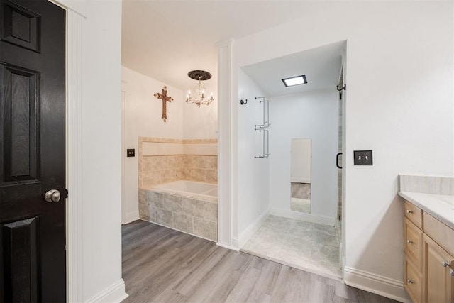 bathroom featuring vanity, wood-type flooring, tiled bath, and an inviting chandelier