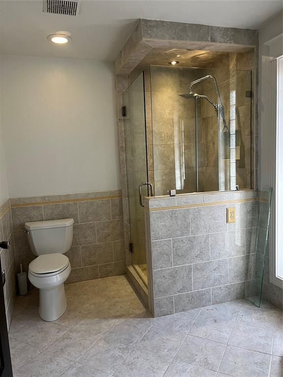 bathroom with tile patterned flooring, toilet, tile walls, and walk in shower