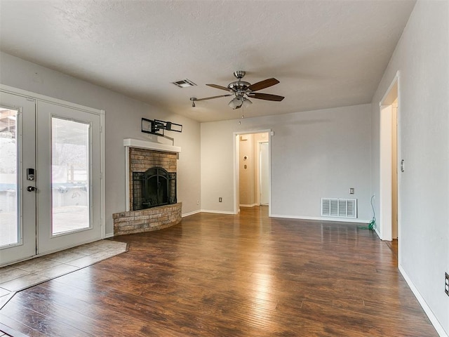 unfurnished living room with french doors, a brick fireplace, ceiling fan, a textured ceiling, and dark hardwood / wood-style flooring