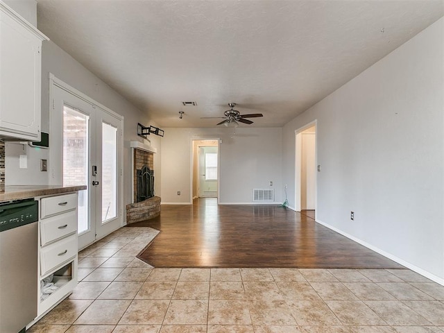 unfurnished living room featuring ceiling fan, light tile patterned floors, and a brick fireplace