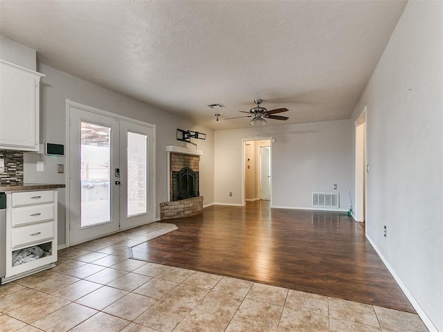 unfurnished living room featuring ceiling fan, light tile patterned floors, a fireplace, and french doors