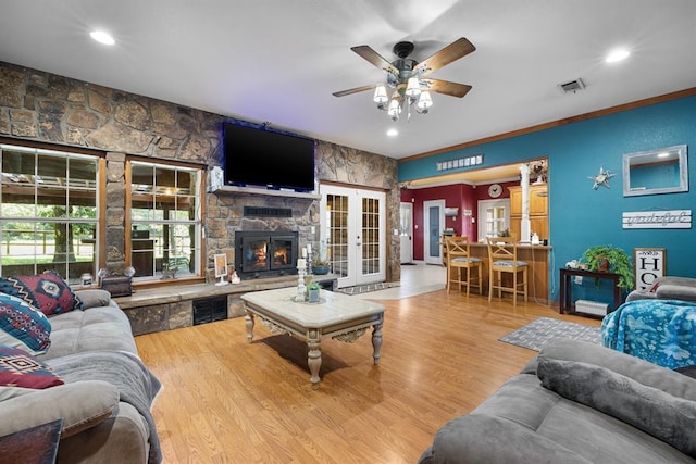 living room featuring french doors, a stone fireplace, ceiling fan, and light hardwood / wood-style flooring