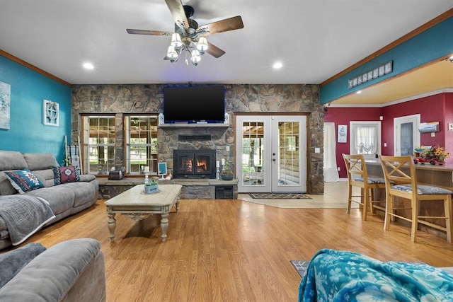 living room featuring french doors, crown molding, a healthy amount of sunlight, a fireplace, and light hardwood / wood-style floors