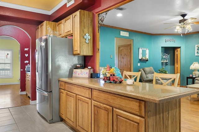 kitchen featuring stainless steel fridge, a breakfast bar area, ceiling fan, ornamental molding, and light tile patterned flooring