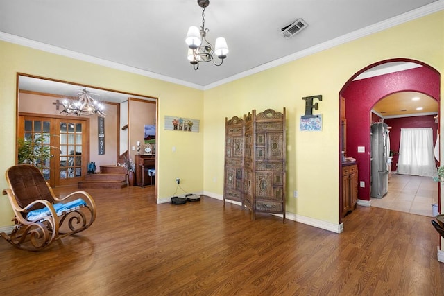 living area with an inviting chandelier, hardwood / wood-style flooring, ornamental molding, and french doors