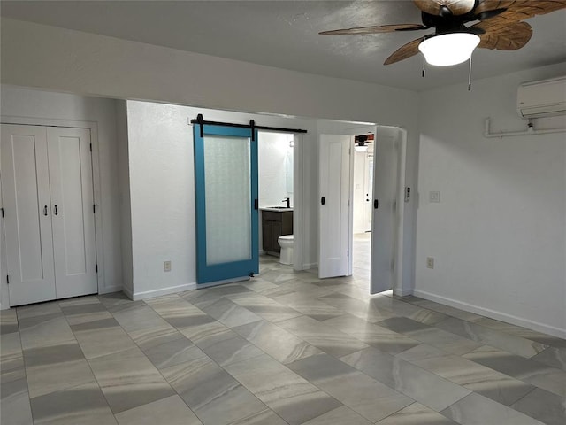 unfurnished bedroom featuring a wall unit AC, ceiling fan, a barn door, ensuite bath, and a closet