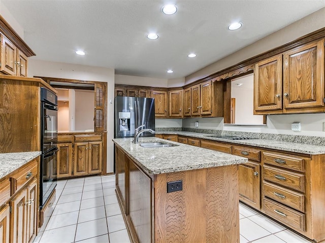 kitchen with stainless steel fridge, light stone counters, sink, light tile patterned floors, and an island with sink