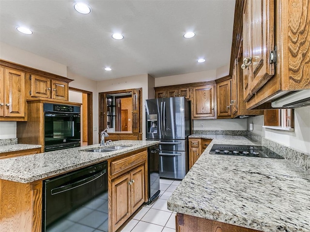 kitchen with light stone countertops, sink, an island with sink, and black appliances