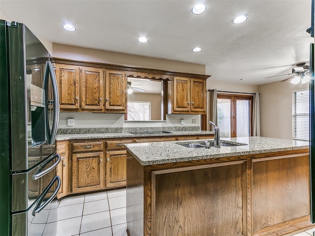 kitchen featuring sink, black fridge, light stone counters, a kitchen island with sink, and light tile patterned floors