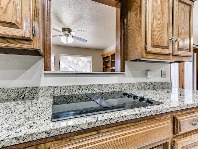 kitchen featuring ceiling fan, black electric stovetop, light stone countertops, and a textured ceiling