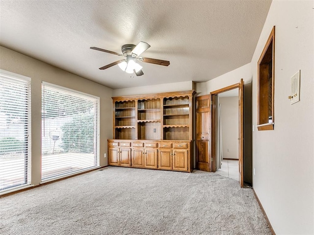 unfurnished living room with ceiling fan, light colored carpet, and a textured ceiling