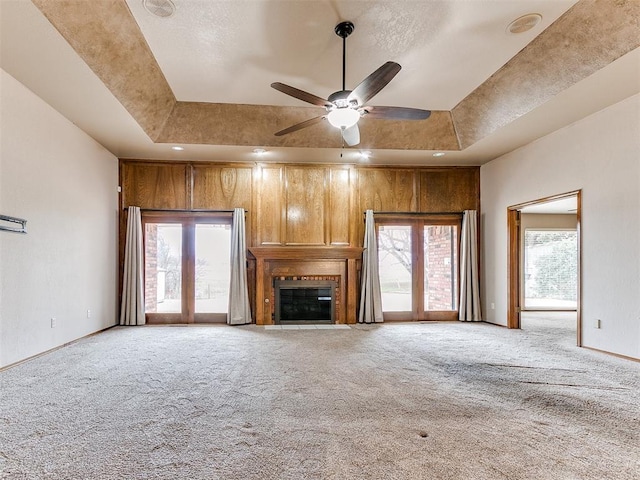 unfurnished living room featuring light carpet, a raised ceiling, ceiling fan, and wood walls