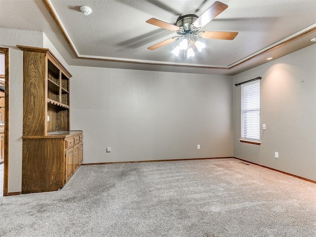 empty room featuring a textured ceiling, carpet floors, a tray ceiling, and ceiling fan